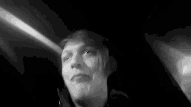 a black and white photo of a person in a dark room looking up at the camera .