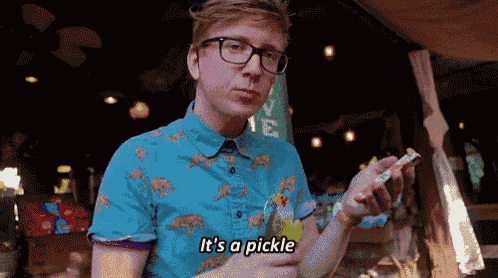 a man wearing glasses and a blue shirt says it 's a pickle while holding a candy bar