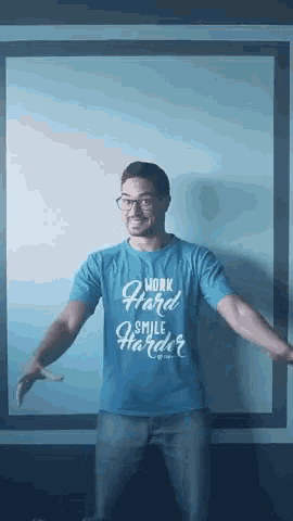 a man wearing a blue shirt that says work hard smile harder is standing with his arms outstretched