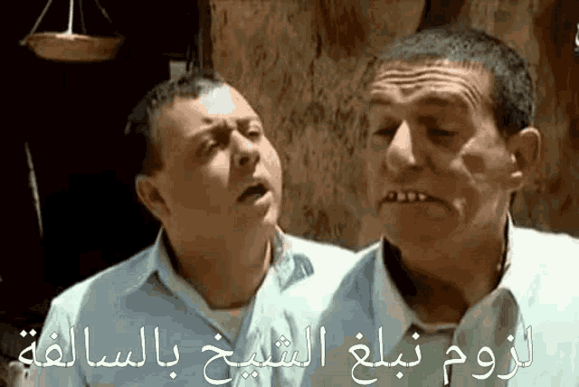 two men are standing next to each other with arabic writing on the bottom of the image .
