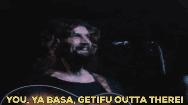 a man with a beard is singing into a microphone while holding a guitar .