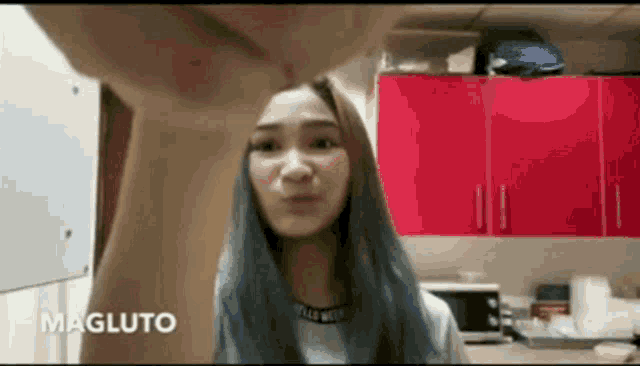 a woman is standing in a kitchen with red cabinets and a microwave .