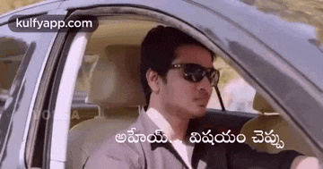 a man wearing sunglasses is driving a car with a caption in telugu .