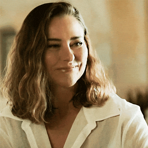a woman in a white shirt is smiling and looking away from the camera