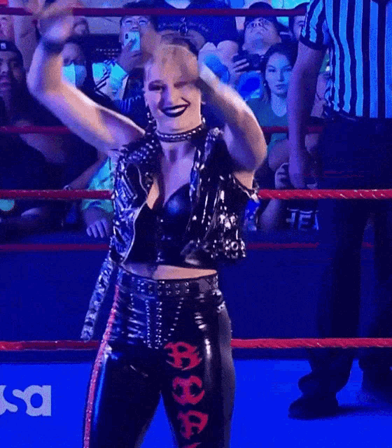 a woman in a wrestling ring is wearing a black outfit with the letter a on the pants
