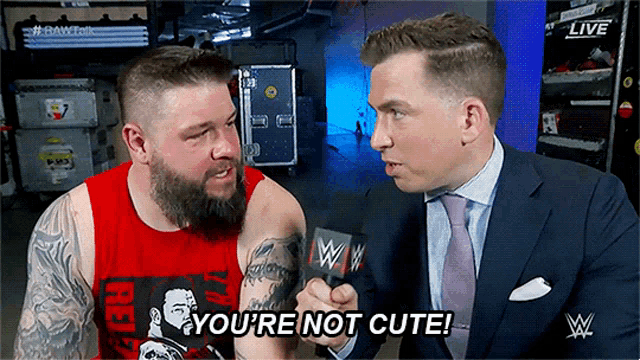a man in a suit and tie is talking to another man with a microphone and says you 're not cute !