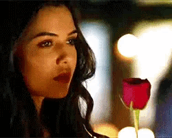 a woman is holding a red rose in a glass