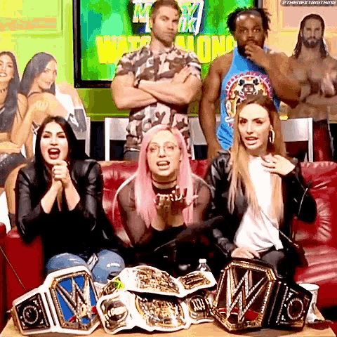 a group of people are sitting on a couch with wrestling championship belts on the table