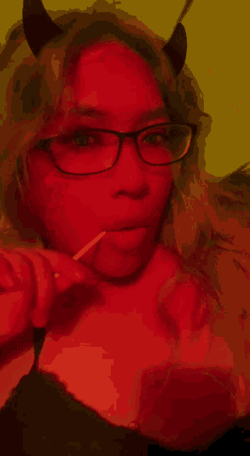 a woman with horns and glasses is holding a lollipop in her mouth