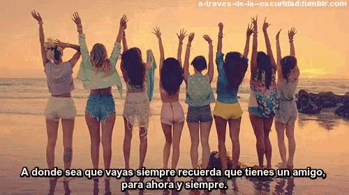 a group of girls are standing on a beach with their hands in the air
