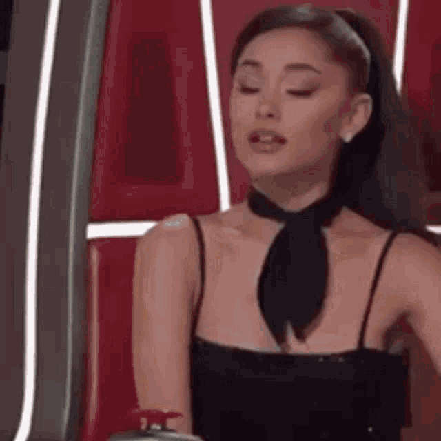 ariana grande is wearing a black dress and a black neck tie .