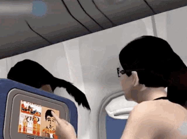 a woman is sitting on an airplane looking at a tv screen with a picture of a man on it