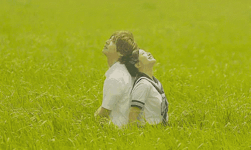 a man and a woman are sitting back to back in a grassy field looking up at the sky .