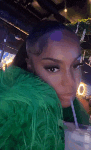 a woman in a green jacket is drinking from a glass with a straw .