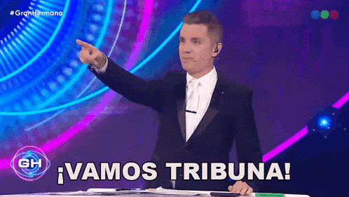 a man in a tuxedo is pointing at something and the words vamos tribuna are on the screen