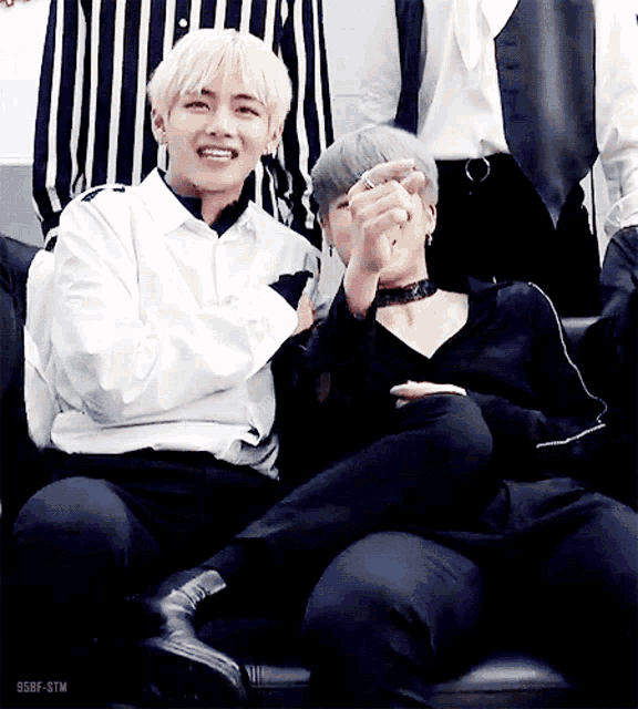 two boys are sitting next to each other on a couch and one of them is wearing a choker .