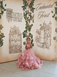 a little girl in a pink dress stands in front of an enchanted forest sign
