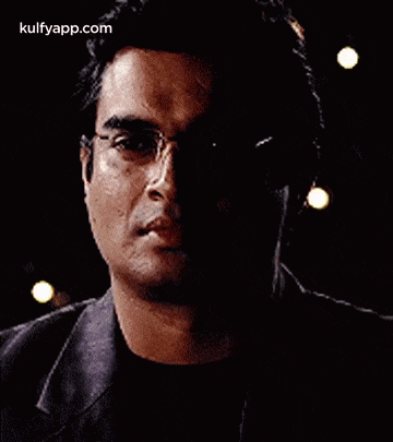 a man wearing glasses and headphones is standing in the dark .