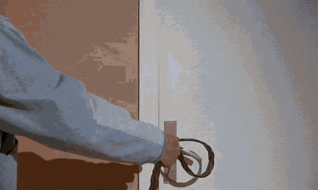 a man in a blue shirt is opening a door with a rope around his waist