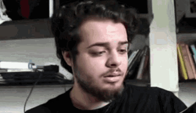 a man with a beard is wearing headphones while sitting in front of a bookshelf .