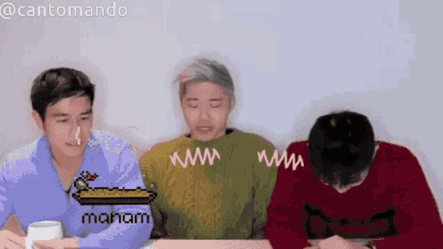 three men are sitting at a table and one of them is wearing a green sweater that says maham on it
