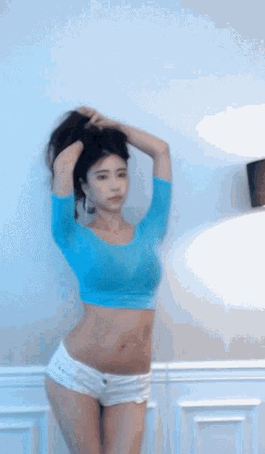 a woman in a blue crop top and white shorts is standing in a room .