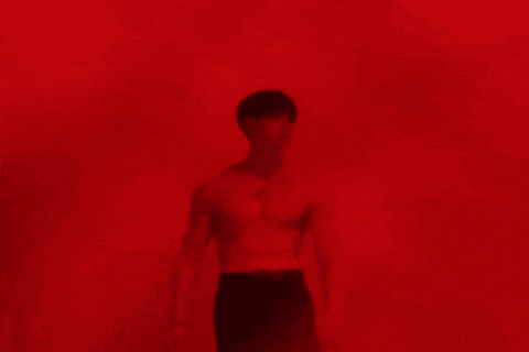 a man is standing in front of a red wall without a shirt on .