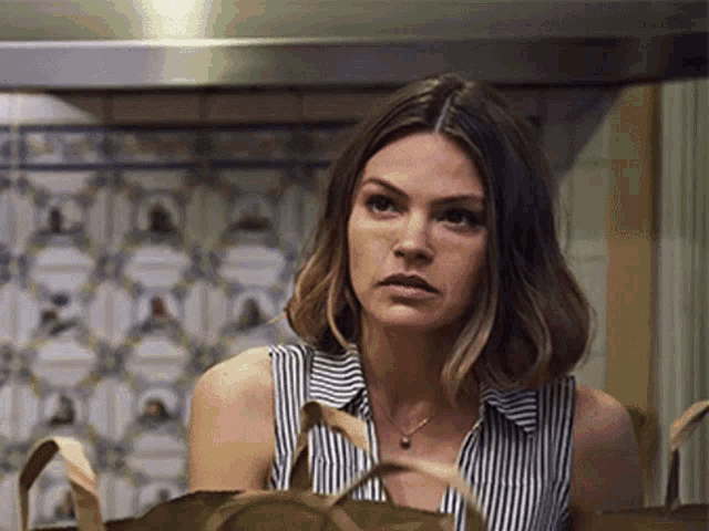 a woman in a striped shirt is holding a bag and looking at the camera