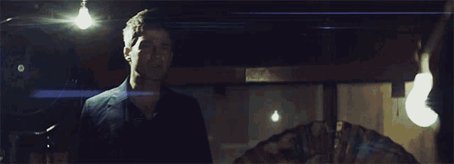 a man in a suit stands in a dark room with a light shining on him