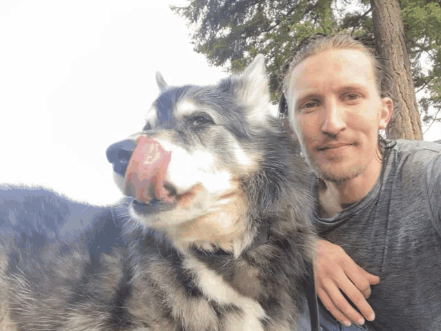 a man and a dog are posing for a picture and the dog is licking its nose