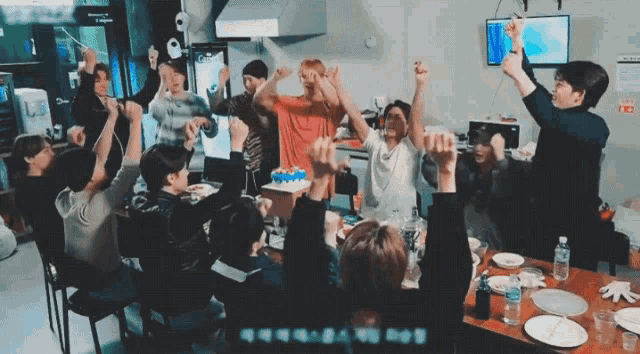 a group of people are sitting around a table with their hands in the air