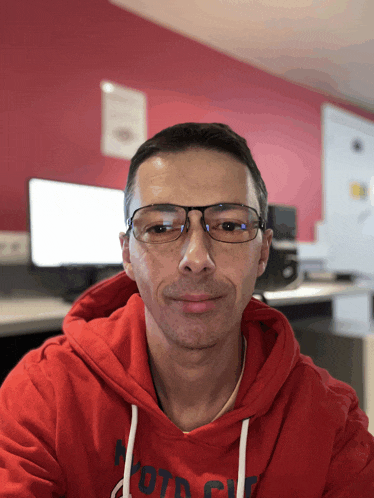 a man wearing glasses and a red hoodie with the word moto on the front