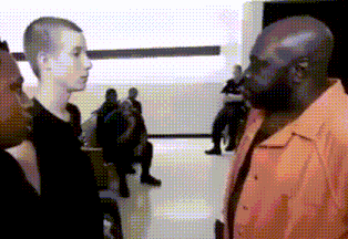 a man in an orange shirt is talking to a boy in a black shirt in a room .