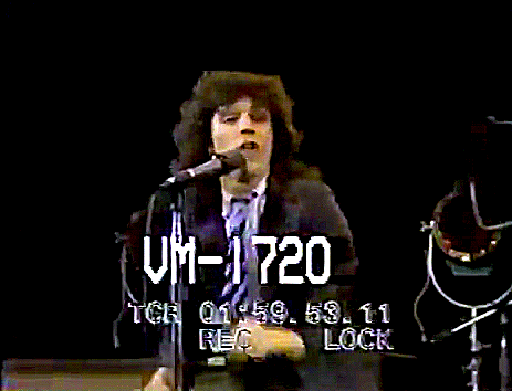 a man in a suit and tie stands in front of a microphone with his arms in the air and says um-1720 in white