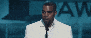 a man in a white suit is speaking into a microphone in front of a sign that says law