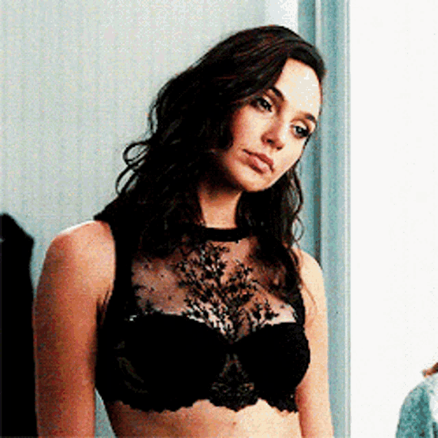 a woman in a black bra is standing in front of a window looking at the camera .