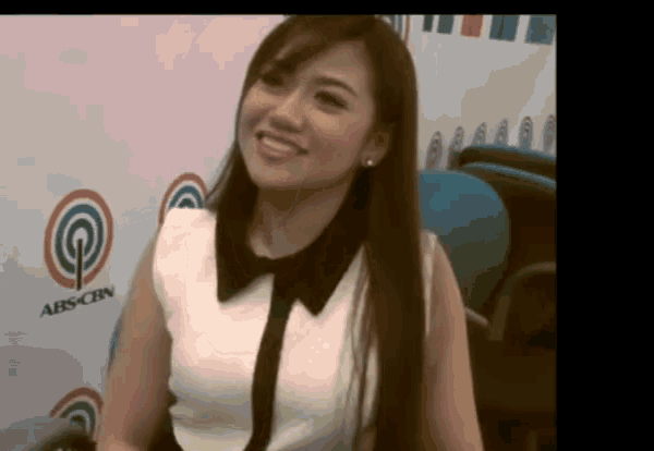 a woman with long hair is smiling in front of an abs cbn logo .
