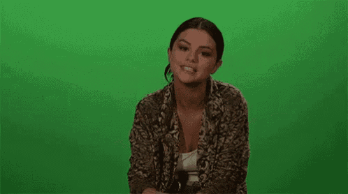 a woman is covering her mouth with her hand while sitting on a green screen .
