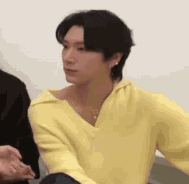 a man wearing a yellow sweater and earrings is sitting next to another man .