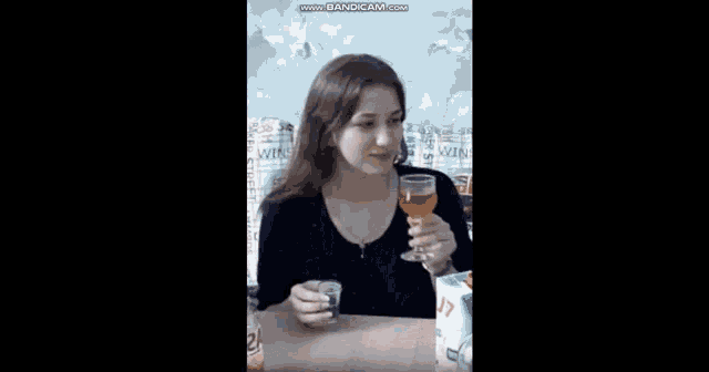 a woman is sitting at a table holding a glass of wine and a bottle of alcohol .