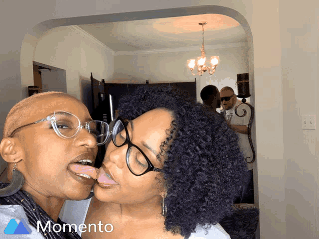 two women are kissing in front of a sign that says " momento "