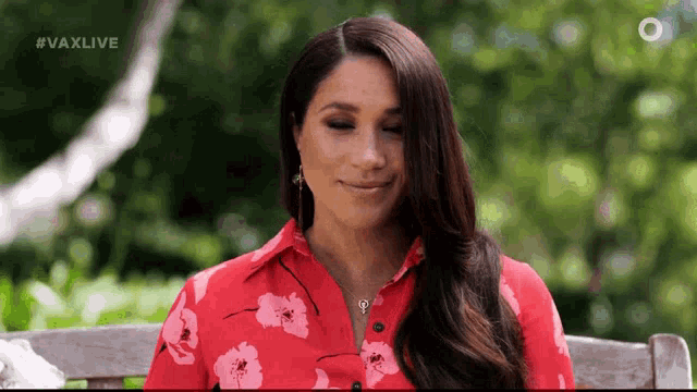 a woman wearing a red floral shirt is sitting on a bench .
