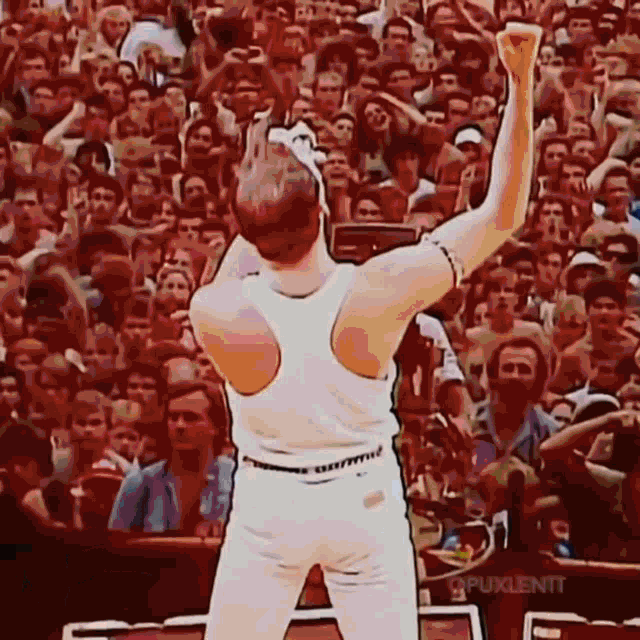 a man in a white tank top stands in front of a crowd with his fist in the air