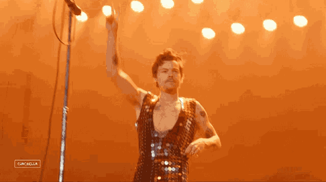 a man in a sequined dress is standing on a stage with his arm up in the air .