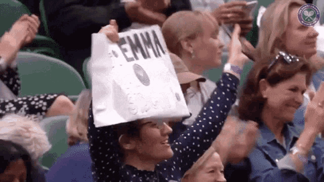 a woman in a crowd holds up a sign that says " emma "