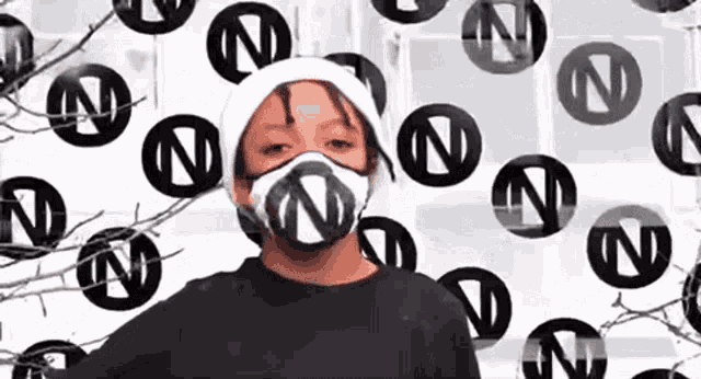 a young boy wearing a mask and a white hat is standing in front of a wall with letters n on it .