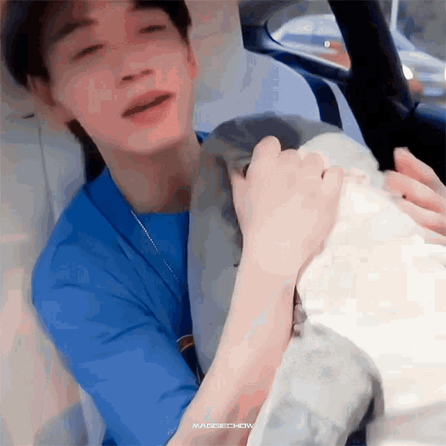 a man in a blue shirt is holding a stuffed animal in his lap in a car .