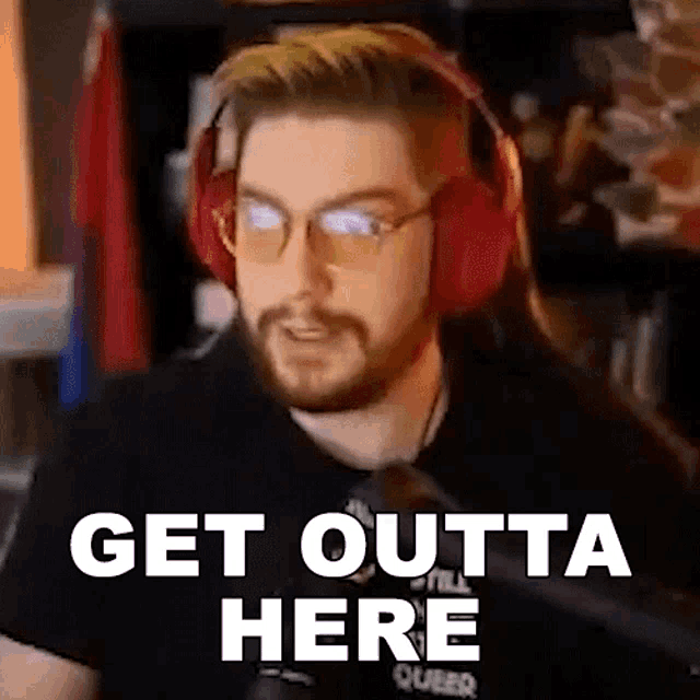 a man wearing headphones and glasses is sitting in front of a computer and says get outta here .