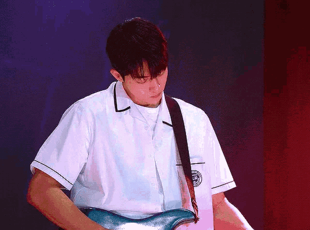 a young man in a white shirt is playing a guitar