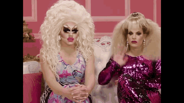 two drag queens are sitting on a couch and one is wearing a pink sequined dress